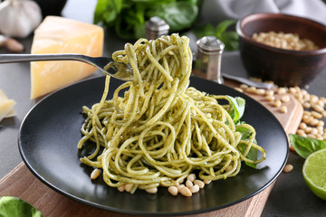 Delicious pasta on fork with pesto sauce over plate, closeup