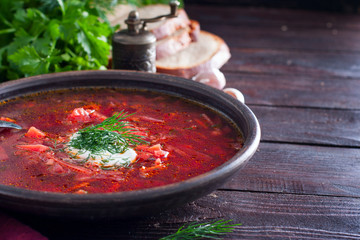 National traditional Ukrainian soup made from beets and vegetables - borscht with sour cream and fresh herbs in a clay bowl, horizontal, copy space