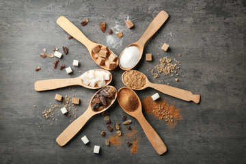 Various kinds of sugar in wooden spoons on grey table