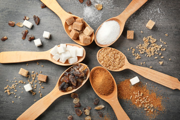 Various kinds of sugar in wooden spoons on grey table