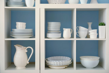 Fototapeta na wymiar White storage stand with ceramic dishware on color background