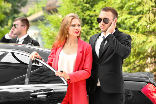 Young businesswoman with bodyguards near car outdoors
