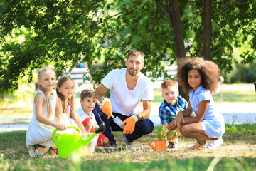 Group of children with teacher planting sapling in park