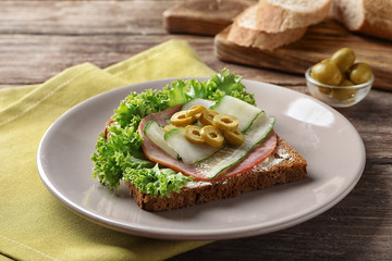 Plate of tasty sandwich with fresh cucumber on table