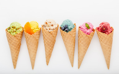 Various of ice cream flavor in cones blueberry ,strawberry ,pistachio ,almond ,orange and cherry setup on white wooden background . Summer and Sweet menu concept.