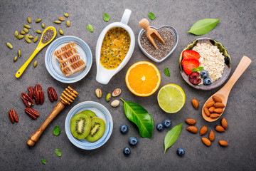 Ingredients for the healthy foods background Mixed nuts, honey, berries, fruits, blueberry, orange, almonds, oatmeal and chia seeds .The concept of healthy food set up on dark stone background.