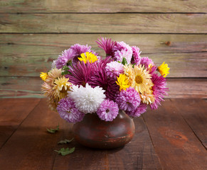 Colorful chrysanthemums bunch in old clay pot on rustic wooden table.