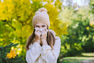 Young woman sneezes in a handkerchief on the street in autumn