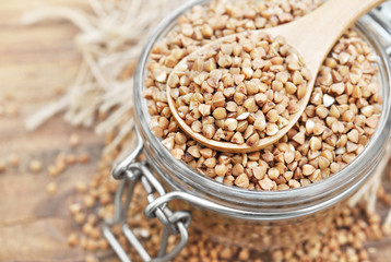 Wooden spoon of roasted buckwheat on groat jar background, gluten free ancient grain for healthy...
