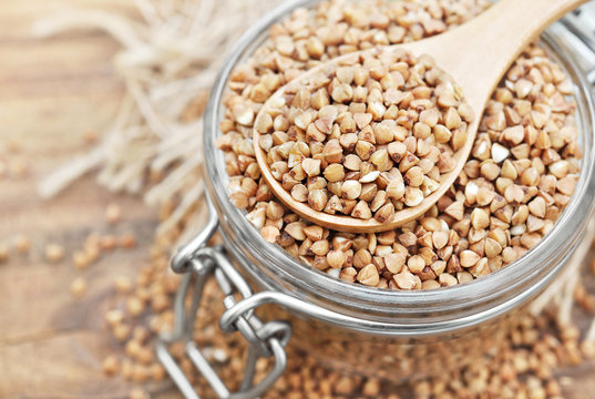 Wooden spoon of roasted buckwheat on groat jar background, gluten free ancient grain for healthy diet