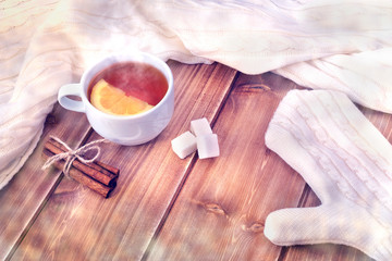 Tea with lemon in white cup, knitted woolen scarf and mitten on a wooden table, frost effect