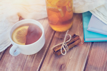 Tea in cup and glasses bottle, books and white knitted woolen scarf on wooden table with frost or rime, winter time
