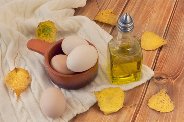 Olive oil in glass bottle and eggs on the scarf on wooden table with yellow autumn leaves