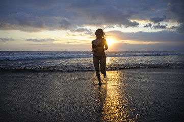 Silhouette of young happy sexy Asian woman in bikini running excited on sunset beach