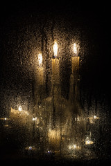 Candles and bottles behind a wet glass on a dark background.