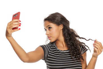 Naklejka premium Young and beautiful dark skinned girl taking a selfies with her smartphone