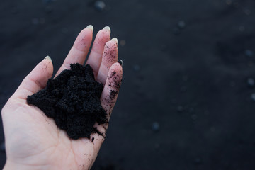 Black volcanic sand in the hands of the traveler. Iceland, beach of Vik. view from the top
