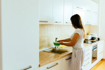 Housewife in pajamas washing cherry tomatoes in household sink to rid off pesticides. Healthy homemade food and cooking concept.