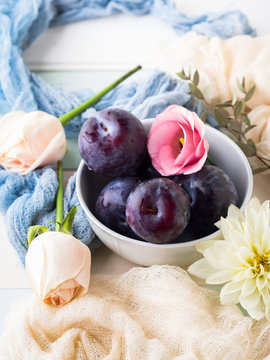 Blue plums in bowl with pink flowers. Summer autumn fruit