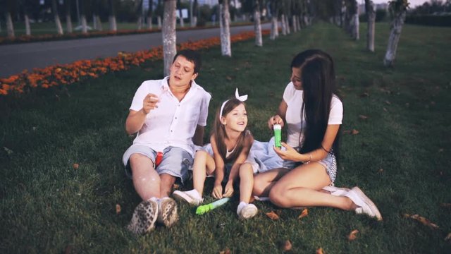 father, mother and girl blowing soap bubbles in city park