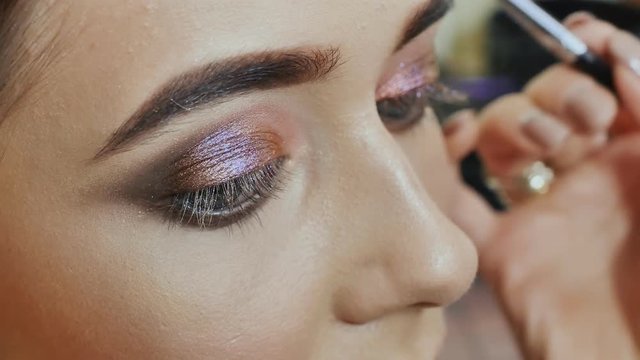 Girl makeup artist paints the eyes of the girl model. Stroke of upper eyelids.