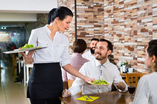 Female waiter bringing order to visitors in country restaurant
