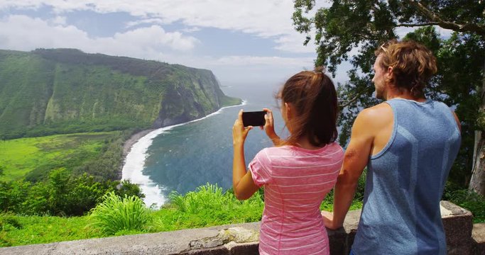 Tourists couple taking photo using phone app at Waipio Valley Lookout Big Island Hawaii landscape. Couple on travel by Hawaiian nature at famous tourist destination on Big Island, Hawaii, USA.