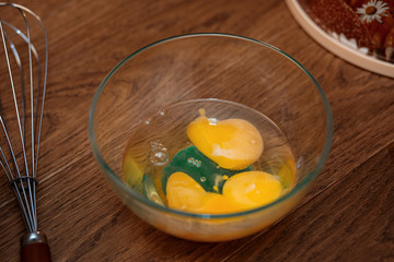 Broken eggs in a transparent bowl and a corolla next to a wooden table