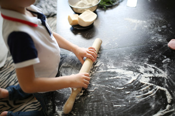 child with dough and rolling pin in real interior