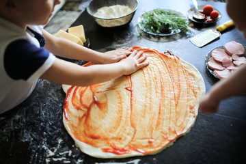 boy prepares pizza with tomato paste,real interior © natalialeb