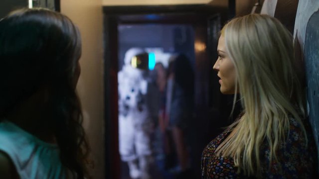  2 girls talking in nightclub, funny astronaut making a move on one of them