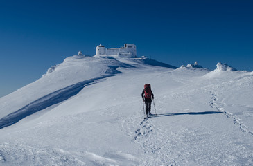 Fototapeta na wymiar Winter picture of a hiker walking towards the abandoned observatory atop the mountain Pip Ivan in Ukrainian Carpathians
