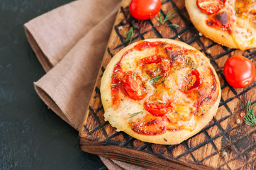 Mini pizzas margheritas on served on a wooden board. Black stone background