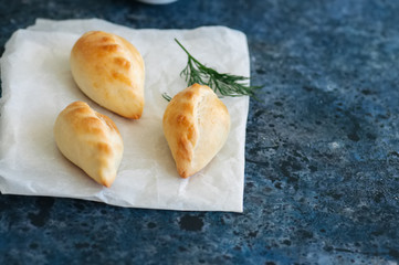 Small mashed potato pasties (hand pies) in a white bowl on a baking paper. Blue stone background.