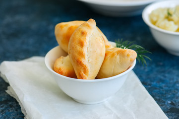 Small mashed potato pasties (hand pies) in a white bowl on a baking paper. Blue stone background.