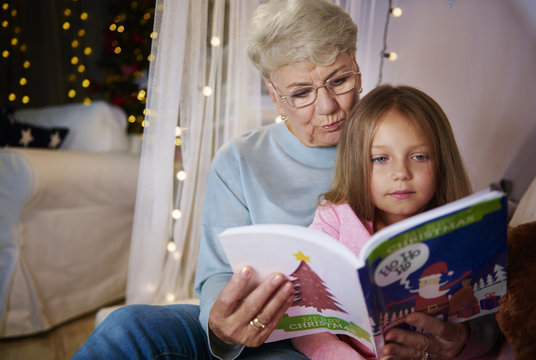 Grandmother and granddaughter reading storybook in bed