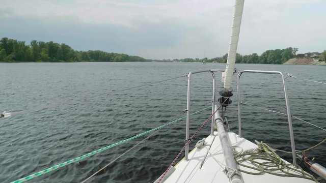 Slow motion view from yacht fore on river-bank and water. Close up of bowsprit and jib furler