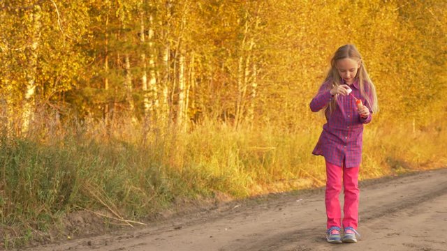 Happy young caucasian girl blowing soap-bubbles outdoors. Golden autumn trees background.