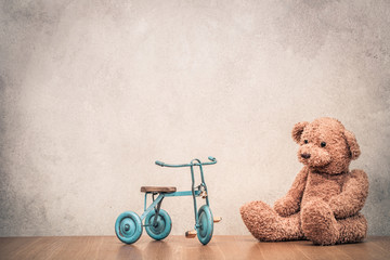 Retro Teddy Bear and old toy trike bicycle front concrete textured wall background. Vintage style...