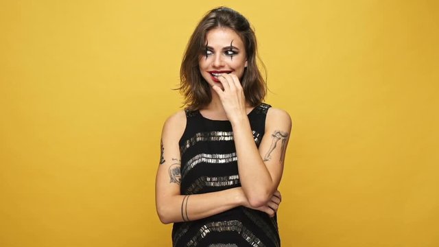 Scary tricky woman with haloween make up thinking about jokes and laughing isolated over yellow
