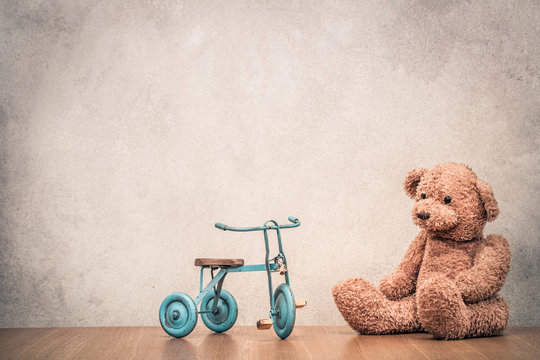 Retro Teddy Bear and old toy trike bicycle front concrete textured wall background. Vintage style filtered photography