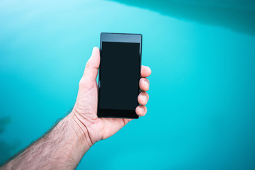 Man holding mobile phone by the swimming pool