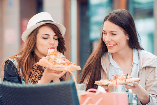 Two beautiful young girls sitting in a cafe and eating pizza