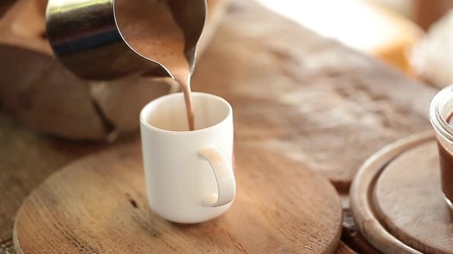 Pouring hot cocoa drink into glass cup on kitchen table.