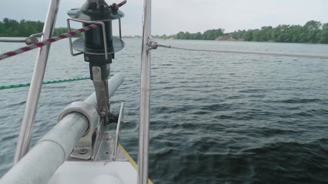 Slow motion view from yacht fore on river-bank and water. Close up of bowsprit and jib furler