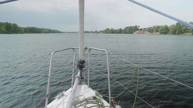 Slow motion view from yacht fore on river-bank and water. Close up of bowsprit and jib furler