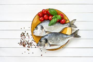 Raw fresh dorado fish on yellow plate and vegetables on white table. Top view copy space