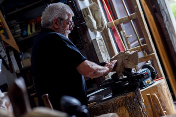 Obraz na płótnie Canvas Senior man working on his wooden sculpture in his workshop.