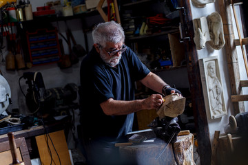 Senior man working on his wooden sculpture in his workshop.