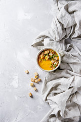 Bowl of vegetarian pumpkin carrot soup served with croutons and onion on textile linen over gray concrete background. Top view with copy space